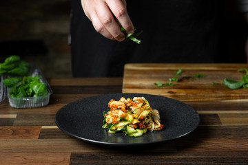 Chef cooking zucchini Italian dish cooking with cheese and tomato sauce, steps on black background kitchen.
