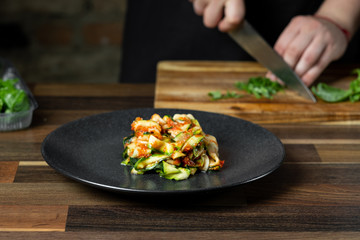 Chef cooking zucchini Italian dish cooking with cheese and tomato sauce, steps on black background kitchen.