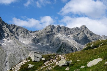 Fototapeta na wymiar panorama montagna cielo azzurro nubi cime rocce parco alpi neve prato verde sentiero