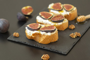Ricotta sandwiches, fresh figs, walnuts and honey on a slate plate on a black background