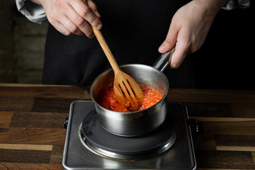 Cooking tomato sauce in metal saucepan by man cook hands, steps process on black background copy text recipe.