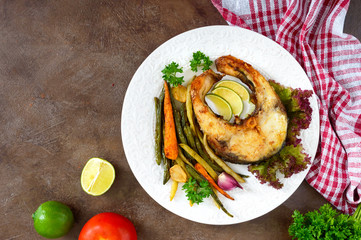 Fried fish steak with grilled vegetables on a white plate. Proper nutrition. Top view.
