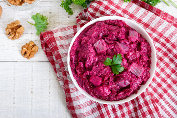 Delicious salad with boiled beets, herring, nuts, onions in a white ceramic bowl. Top view.