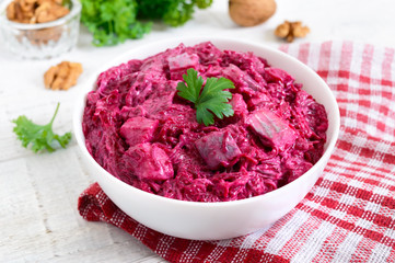 Delicious salad with boiled beets, herring, nuts, onions in a white ceramic bowl.
