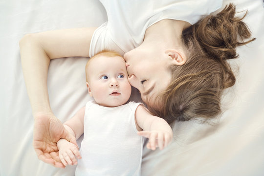Top view of a happy mother kissing a baby lying on a bed indoors.