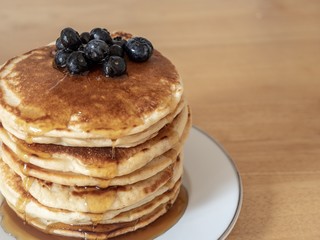 A large stack of pancakes covered with maple syrup and blue berries