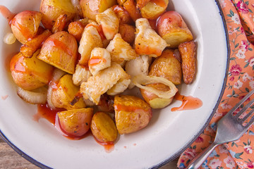 Traditional farmers food. Roasted red potatoes with carrots, onions and chicken breast pieces in old metal plate on wooden background. Served with red tomatoes and a mug of clean water. Tasty meal