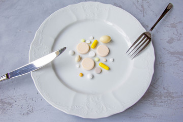 Plate full of pills of different sizes, shapes and colors served as a dinner with silver knife and fork