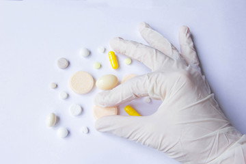 Fototapeta na wymiar Hand in latex glove taking pills from the table. White background