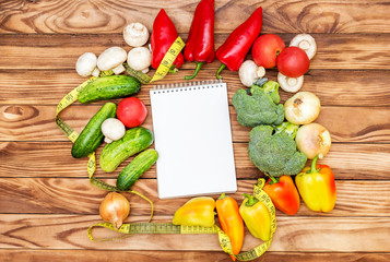 Blank notepad with different vegetables and measure tape on wooden background. Top view. Healthy food concept.
