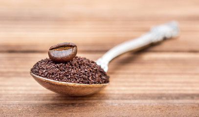 Spoon with ground coffee and coffee bean on the table. Close up.