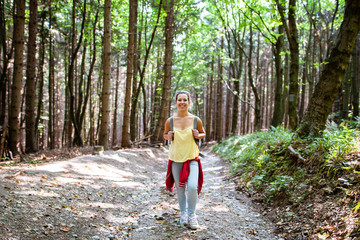 Naklejka na ściany i meble Beautiful woman smiling at path in a forest during hiking on a hill during sunrise on summer