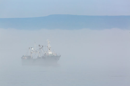 Fototapeta Fishing boat in thick fog on the background of mountains