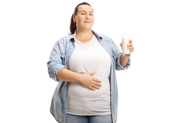 Satisfied overweight woman with a glass of milk holding her hand on her stomach