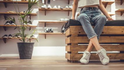 women sitting with legs crossed trying on new sneakers in shopping center