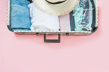 Open suitcase with female clothes for trip on pastel pink. Top view with copy space. Summer concept travel.