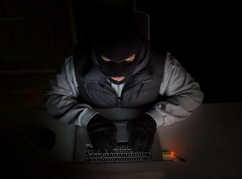 Hacker with balaclava typing on laptop