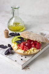 Pita bread sandwich with scrambled eggs, tomato, avocado and herbs on o white wooden cutting board. Delicious breakfast, lunch or snack.