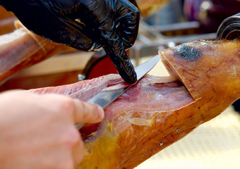 A person cuts serrano ham with a knife