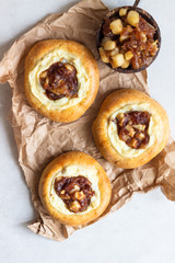Fresh homemade open yeast buns with cottage cheese and caramel apple (traditional Russian pastry vatrushka, round buns, curd tart) on light grey background. Sweet rolls. Selective focus. Rustic style.