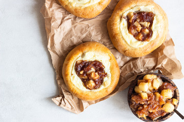 Fresh homemade open yeast buns with cottage cheese and caramel apple (traditional Russian pastry vatrushka, round buns, curd tart) on light grey background. Sweet rolls. Selective focus. Rustic style.