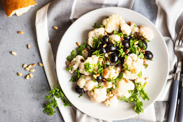 Fresh vegetable salad with cauliflower, olives, parsley and pine nuts in a grey plate on a grey stone background. Healthy food concept