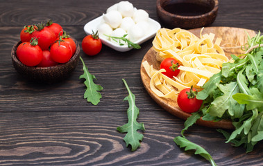 Ingredients for cooking pasta. Tagliatelle, cherry tomatoes, arugula, olive oil and mozzarella on old wooden background. Italian pasta ingredients.