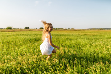adorable little child running by green field under sunset rays