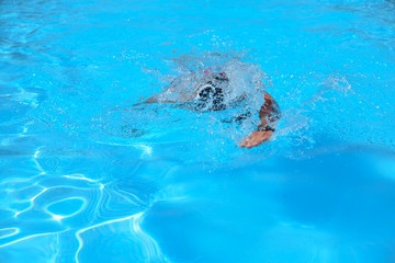 Fototapeta na wymiar Caucasian man swims in freestyle (crawl) at the outdoor swimming pool on a sunny summer day