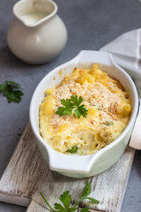 Homemade pasta casserole with fish and green pea in bechamel sauce in a baking dish on a light slate, stone or concrete background. Copy space for text.