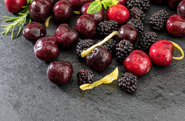 Delicious and appetizing fruits of the forest, blackberries and fresh and raw cherries. On dark background.