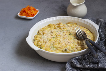 Homemade pasta casserole with fish and green pea in bechamel sauce in a baking dish on a light slate, stone or concrete background. Copy space for text.