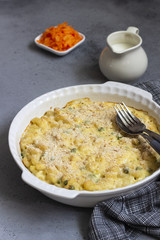 Homemade pasta casserole with fish and green pea in bechamel sauce in a baking dish on a light slate, stone or concrete background. Copy space for text.