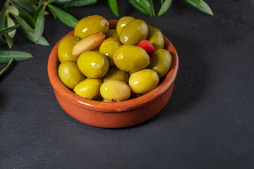 Clay pot with artisan olives (preserved in extra virgin olive oil, vinegar, spices) with red peppers and garlic. Includes leaves of the olive tree. Appetizer concept. On black chalkboard background. S