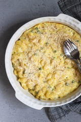 Homemade pasta casserole with fish and green pea in bechamel sauce in a baking dish on a light slate, stone or concrete background. Copy space for text.