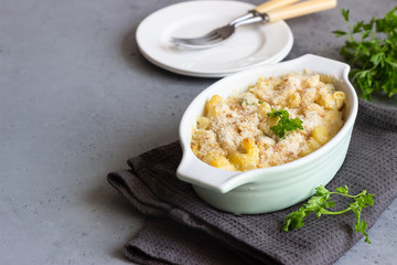 Baked mac and cheese, american style macaroni pasta with cheesy sauce, parsley and crunchy breadcrumbs topping, in portioned ceramic form.