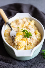 Baked mac and cheese, american style macaroni pasta with cheesy sauce, parsley and crunchy breadcrumbs topping, in portioned ceramic form.