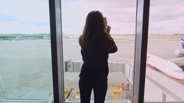 Woman make video on mobile phone at airport back view. Close up of female tourist looking plane arrival. Woman take picture on smartphone at airport. Woman tourist enjoy plane runway view