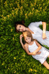 top view of beautiful mother and daughter lying in flowery meadow
