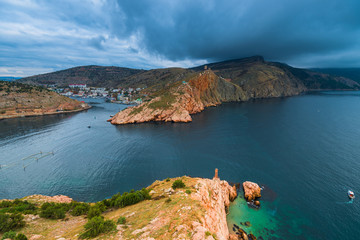 Fototapeta premium Heavy rain clouds over the bay, rocky mountains and city in the bay, seascape