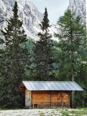Fototapeta na wymiar A picturesque panorama in the Dolomites. There are huge mountains covered with snow, coniferous forests, mountain clear azure lake, a lonely wild place, a deserted hut in the forest
