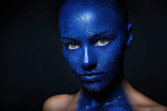 beautiful girl face painted with blue paint with glitter.