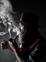 dramatic portrait of senior man in hat smoking tobacco pipe. Profile view of Austrian, Tyrolean, Bavarian old man