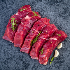 Raw meat, beef steak with seasoning on black stone table, top view