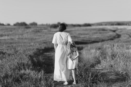 Black And White Shot Of Mother And Daughter Walking By Rural Road In Green Meadow