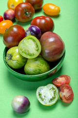 Multicolored assortment of French fresh ripe tomatoes in green bowl on green table