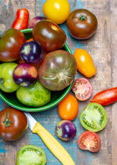 Multicolored assortment of French fresh ripe tomatoes in green bowl on blue wooden table