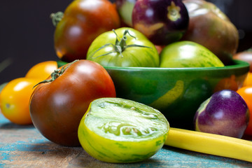 Multicolored assortment of French fresh ripe tomatoes in green bowl on blue wooden table, dark key