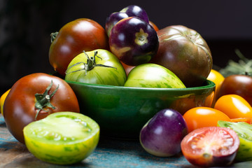 Fototapeta na wymiar Multicolored assortment of French fresh ripe tomatoes in green bowl on blue wooden table, dark key