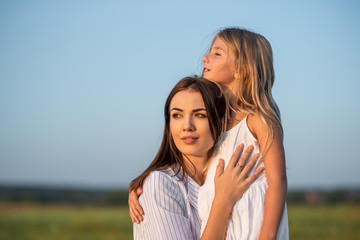 mother and daughter embracing in green meadow and looking away